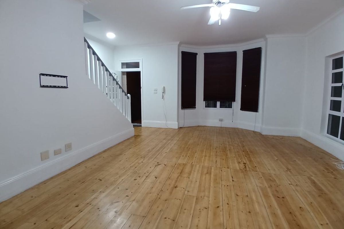 Spacious living area featuring polished timber flooring, a bay window, and a staircase with a classic balustrade.