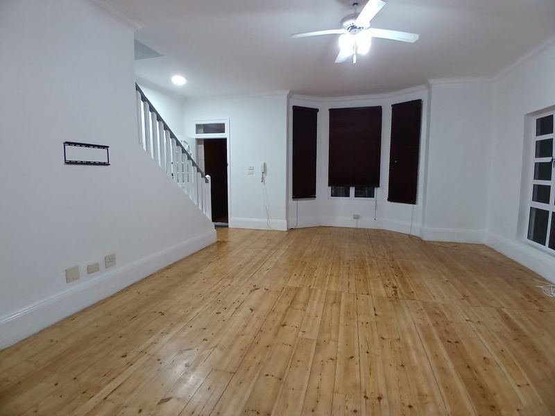 Spacious living area featuring polished timber flooring, a bay window, and a staircase with a classic balustrade.