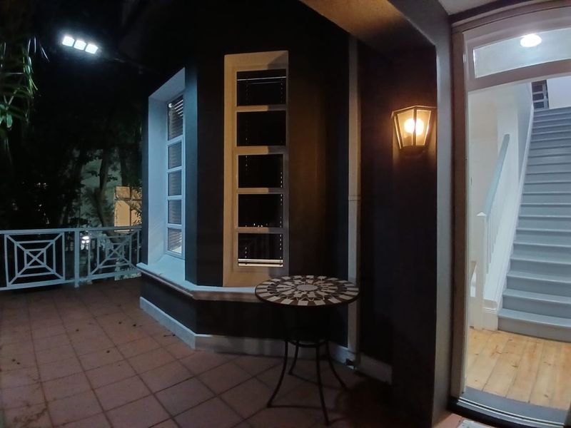 A covered balcony area at night featuring tiled flooring, a bay window, and access to an interior staircase.
