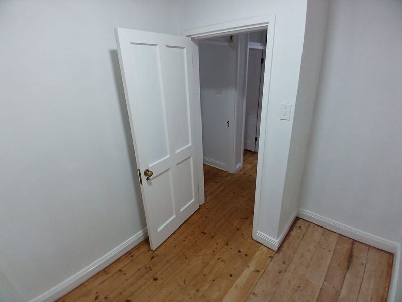 A vacant hallway featuring polished timber flooring and a classic panelled door, leading into an adjacent interior space.