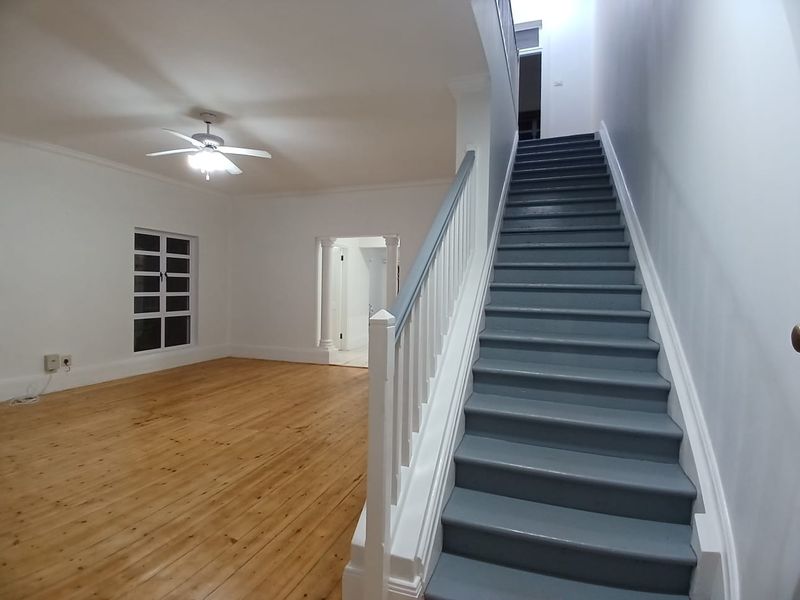 Spacious entrance hall featuring polished wooden flooring, a central staircase with painted treads, and architectural columns leading to adjacent living areas.