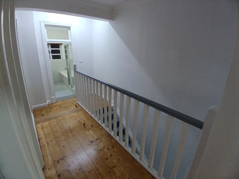 A bright upstairs hallway featuring polished timber flooring and a classic staircase balustrade, leading towards a bathroom.