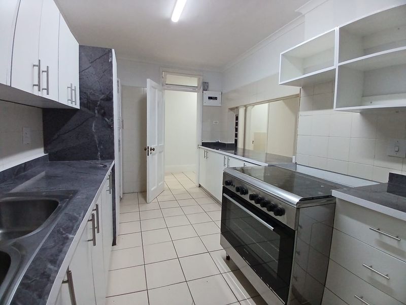 A functional kitchen featuring white cabinetry, dark laminate countertops, a stainless steel sink, and a freestanding stove with tiled flooring.