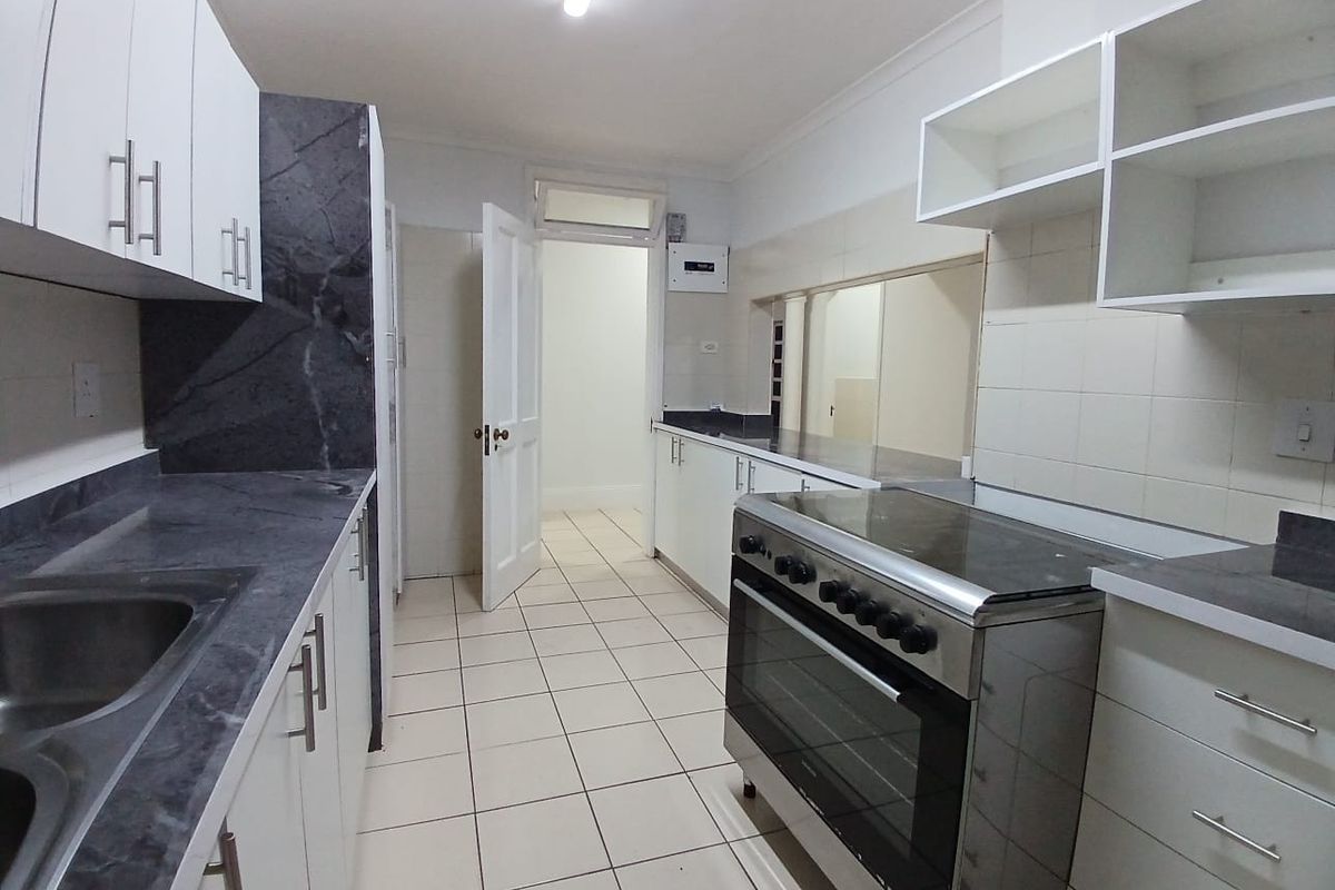A functional kitchen featuring white cabinetry, dark laminate countertops, a stainless steel sink, and a freestanding stove with tiled flooring.