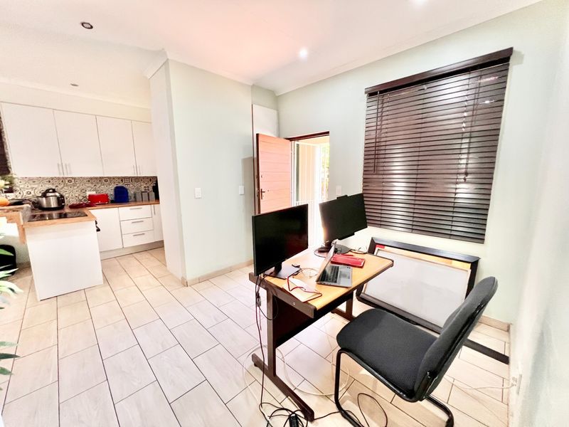 Open-plan living area featuring a functional kitchen with built-in cabinetry and tiled flooring, seamlessly connected to a versatile workspace area.