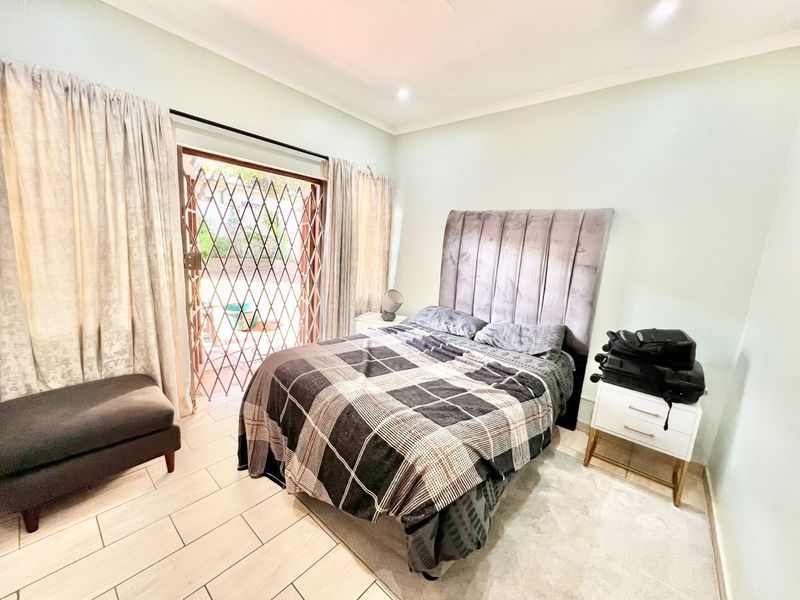A well-lit bedroom featuring tiled flooring, recessed lighting, and a sliding glass door with a security gate providing direct access to the outdoors.