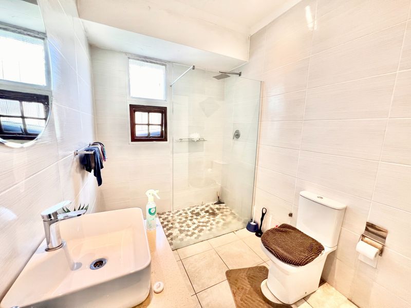 Modern bathroom featuring a walk-in shower with glass screen, vessel sink, and neutral tiled finishes throughout.