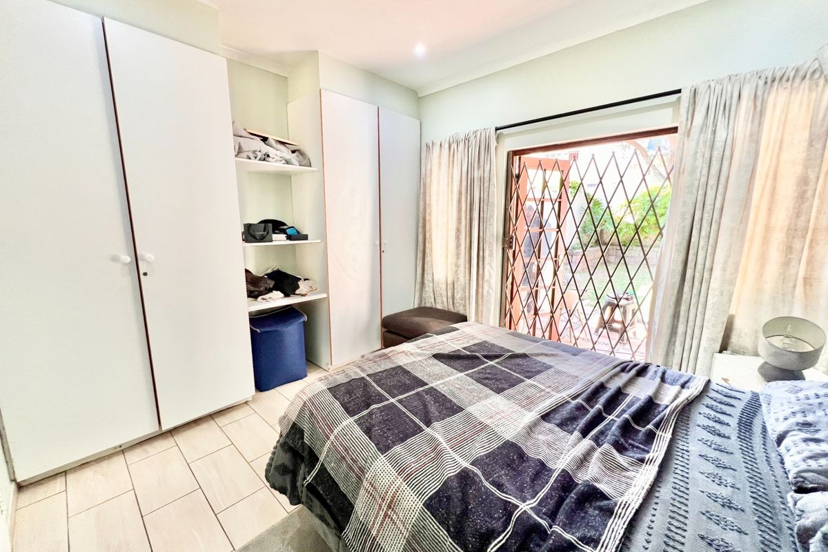 Bedroom featuring built-in cupboards, tiled flooring, and a sliding door with a security gate providing direct access to the garden.