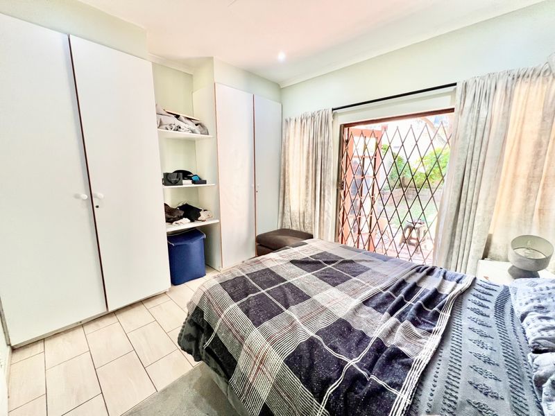 Bedroom featuring built-in cupboards, tiled flooring, and a sliding door with a security gate providing direct access to the garden.