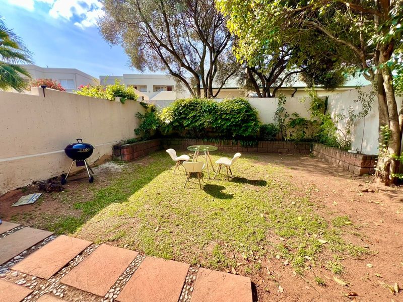 A private rear garden featuring a paved walkway, retaining wall, and boundary wall, offering a quiet outdoor space with established trees.