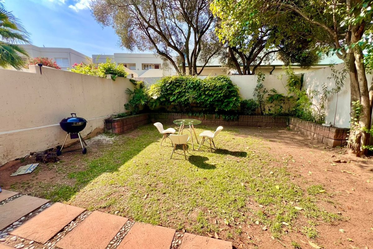 A private rear garden featuring a paved walkway, retaining wall, and boundary wall, offering a quiet outdoor space with established trees.