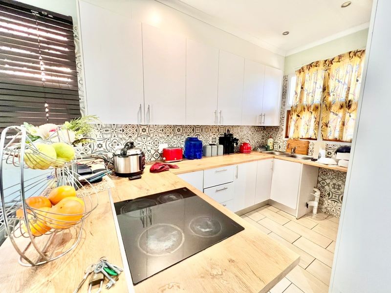 A functional kitchen featuring white cabinetry, wood-look laminate countertops, a built-in electric cooktop, and decorative patterned tile backsplash.