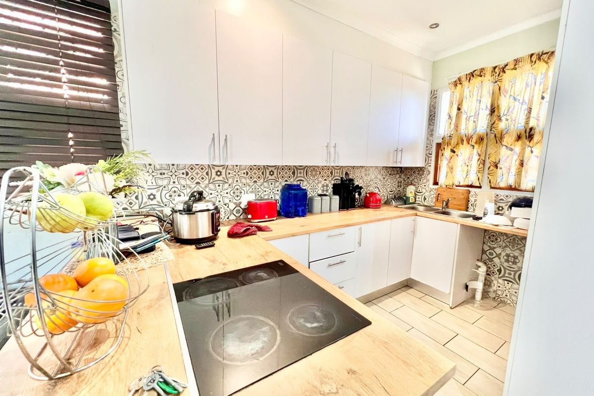 A functional kitchen featuring white cabinetry, wood-look laminate countertops, a built-in electric cooktop, and decorative patterned tile backsplash.