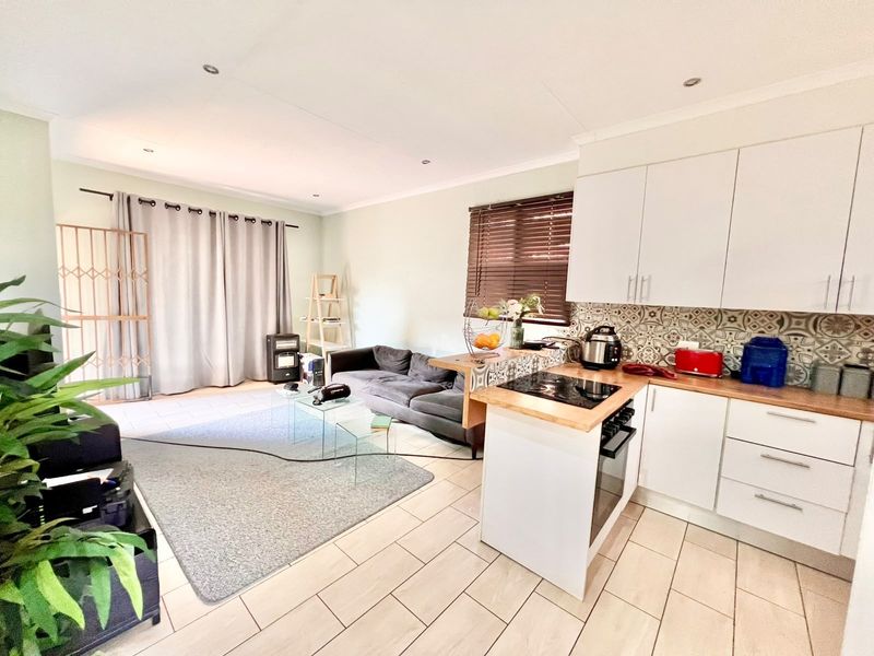 Open-plan living area featuring a modern kitchen with white cabinetry, wooden countertops, patterned backsplash, and tiled flooring throughout the combined space.