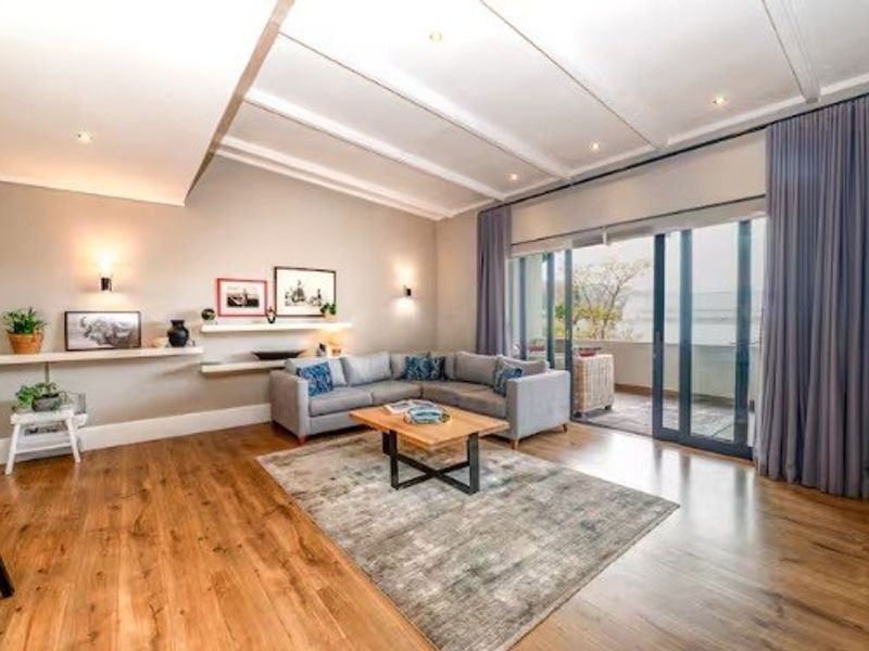 Spacious living room featuring hardwood flooring, recessed ceiling lighting, and large sliding glass doors that open to an outdoor balcony area.