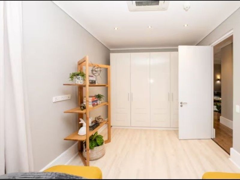 A well-maintained bedroom featuring light laminate flooring, ample built-in cupboard storage, and recessed ceiling lighting with integrated air conditioning.