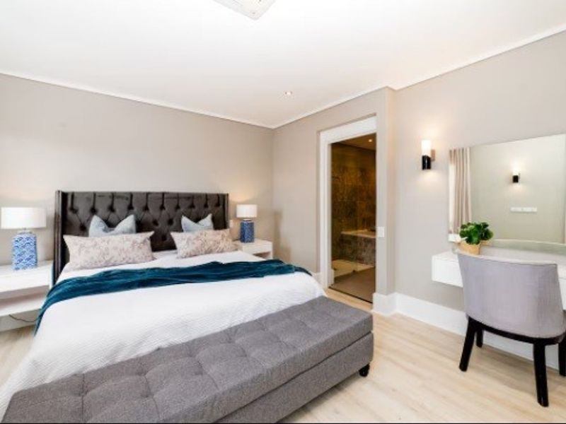 A well-maintained bedroom featuring neutral walls, recessed lighting, laminate flooring, and an integrated wall-mounted vanity, with an adjoining bathroom visible.