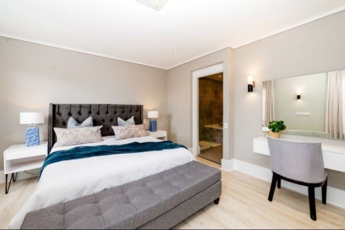 A well-maintained bedroom featuring neutral walls, recessed lighting, laminate flooring, and an integrated wall-mounted vanity, with an adjoining bathroom visible.