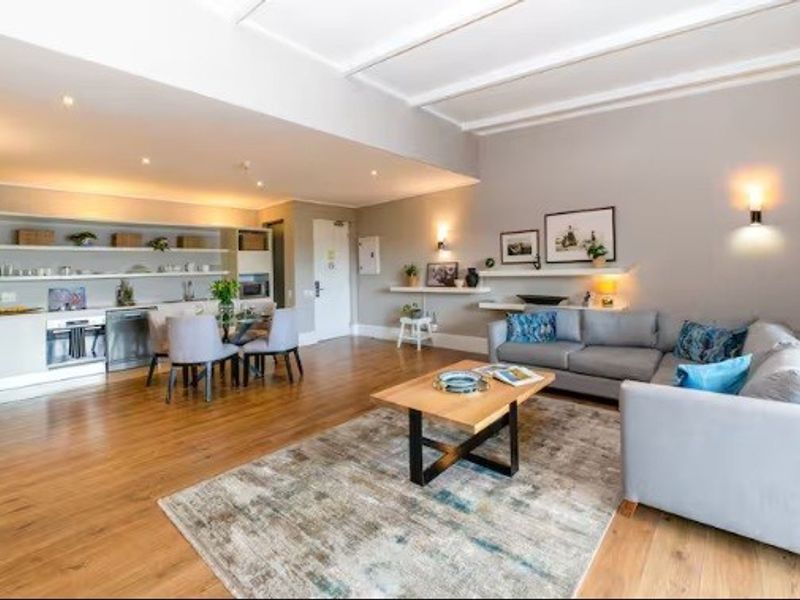 Spacious open-plan living area featuring hardwood flooring, integrated kitchen appliances, built-in shelving, and modern recessed lighting throughout the combined kitchen and lounge space.