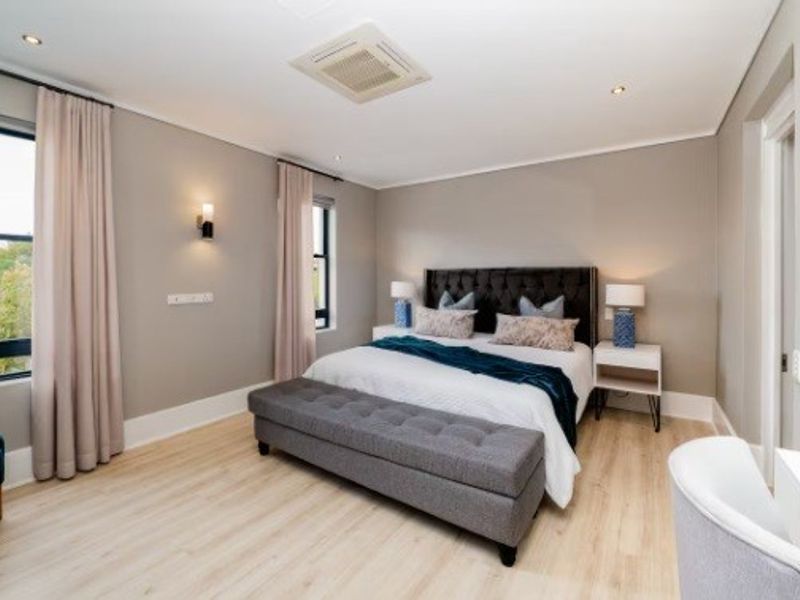 A well-maintained bedroom featuring light laminate flooring, recessed ceiling lighting, ducted air conditioning, and neutral wall finishes.