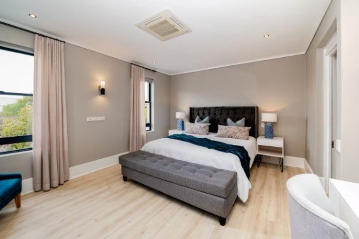 A well-maintained bedroom featuring light laminate flooring, recessed ceiling lighting, ducted air conditioning, and neutral wall finishes.