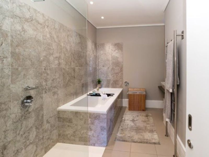 Modern bathroom featuring a built-in bathtub, glass shower screen, and elegant stone-look wall tiling with a heated towel rail.
