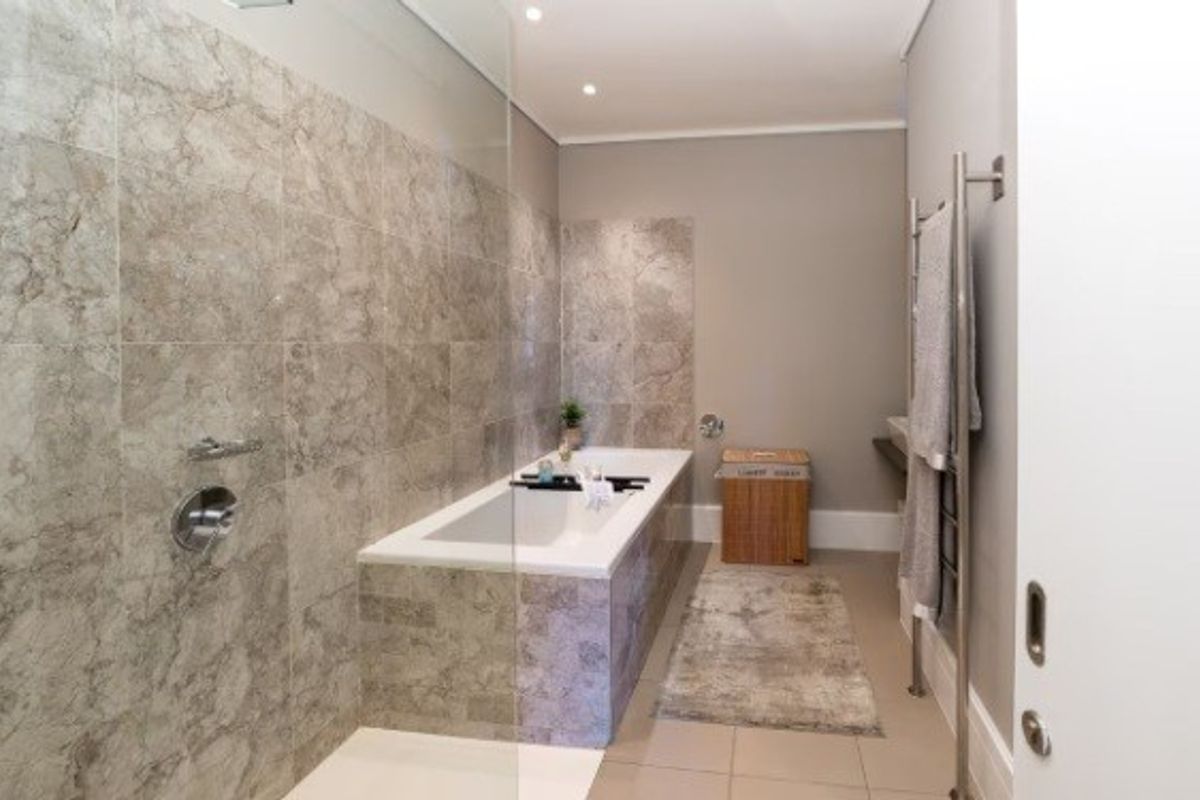 Modern bathroom featuring a built-in bathtub, glass shower screen, and elegant stone-look wall tiling with a heated towel rail.
