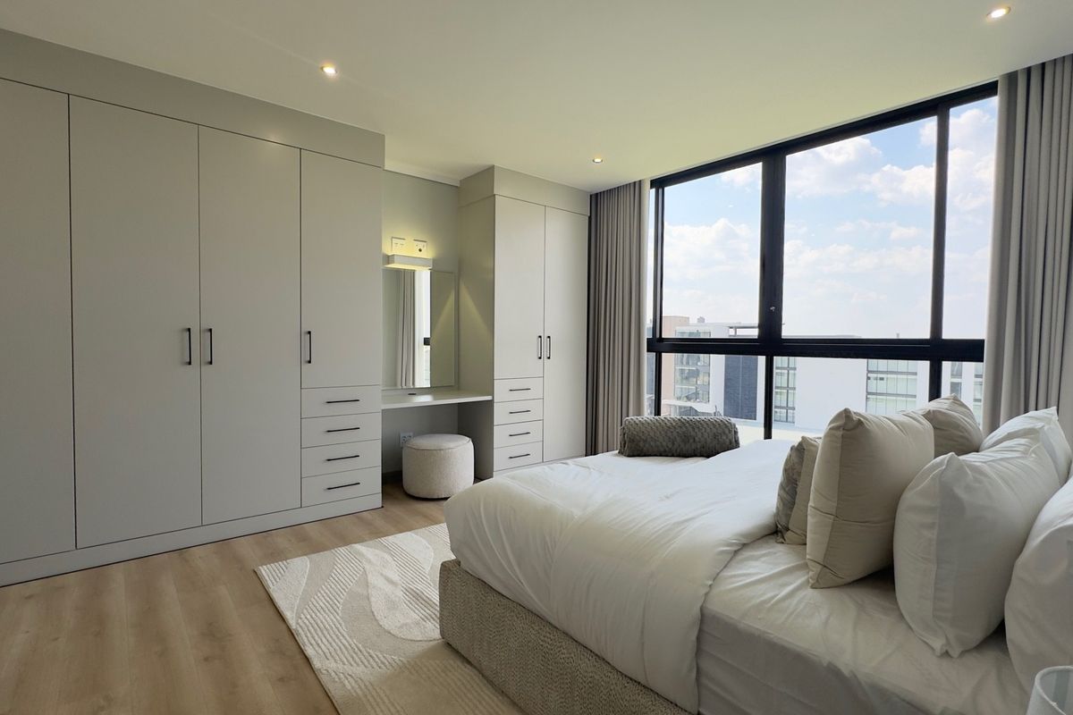 Modern bedroom featuring extensive built-in cabinetry with an integrated vanity, large windows providing natural light, and high-quality laminate flooring.