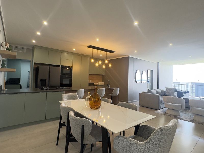 Modern open-plan living area featuring a sleek kitchen with integrated appliances, recessed lighting, and large format floor tiles leading to a balcony.