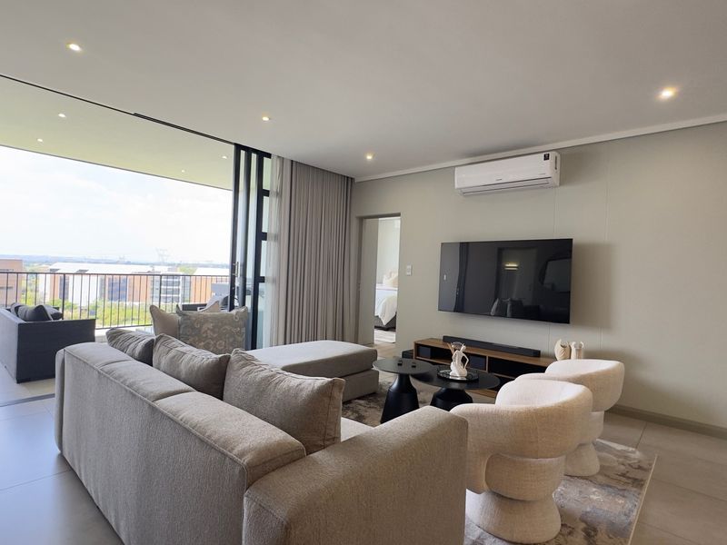 Modern living room featuring tiled floors, recessed lighting, a wall-mounted air conditioner, and large sliding doors opening onto a balcony with urban views.