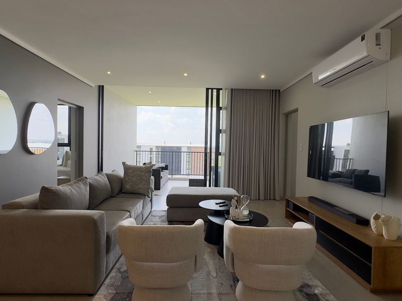Modern open-plan living area featuring recessed lighting, a wall-mounted air conditioning unit, and seamless access to a private balcony through large sliding glass doors.