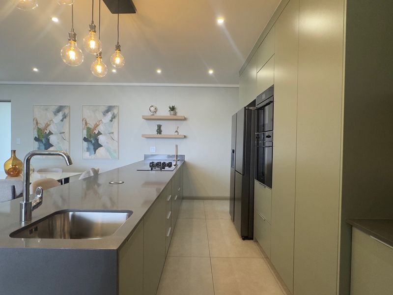 Modern kitchen featuring a large island with stone countertops, integrated cabinetry, built-in oven, and gas hob, complemented by stylish floating shelves and recessed lighting.