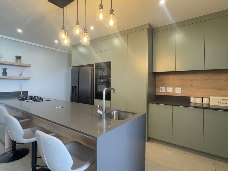 Modern kitchen featuring sage green cabinetry, stone countertops, a central island with integrated hob, and high-quality built-in appliances.