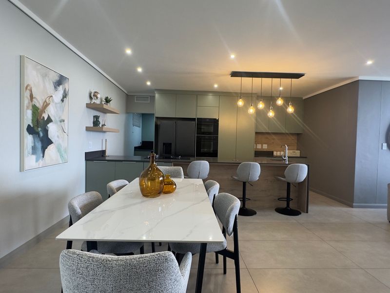 Modern open-plan living area featuring a sleek kitchen with built-in cabinetry, a central island, and contemporary lighting fixtures throughout the space.