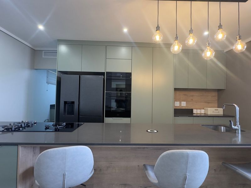 Modern kitchen featuring sage green cabinetry, a large stone island with integrated gas cooktop, built-in oven, and contemporary pendant lighting.