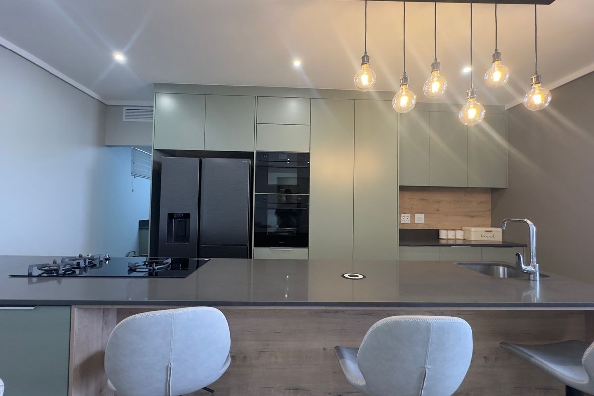 Modern kitchen featuring sage green cabinetry, a large stone island with integrated gas cooktop, built-in oven, and contemporary pendant lighting.