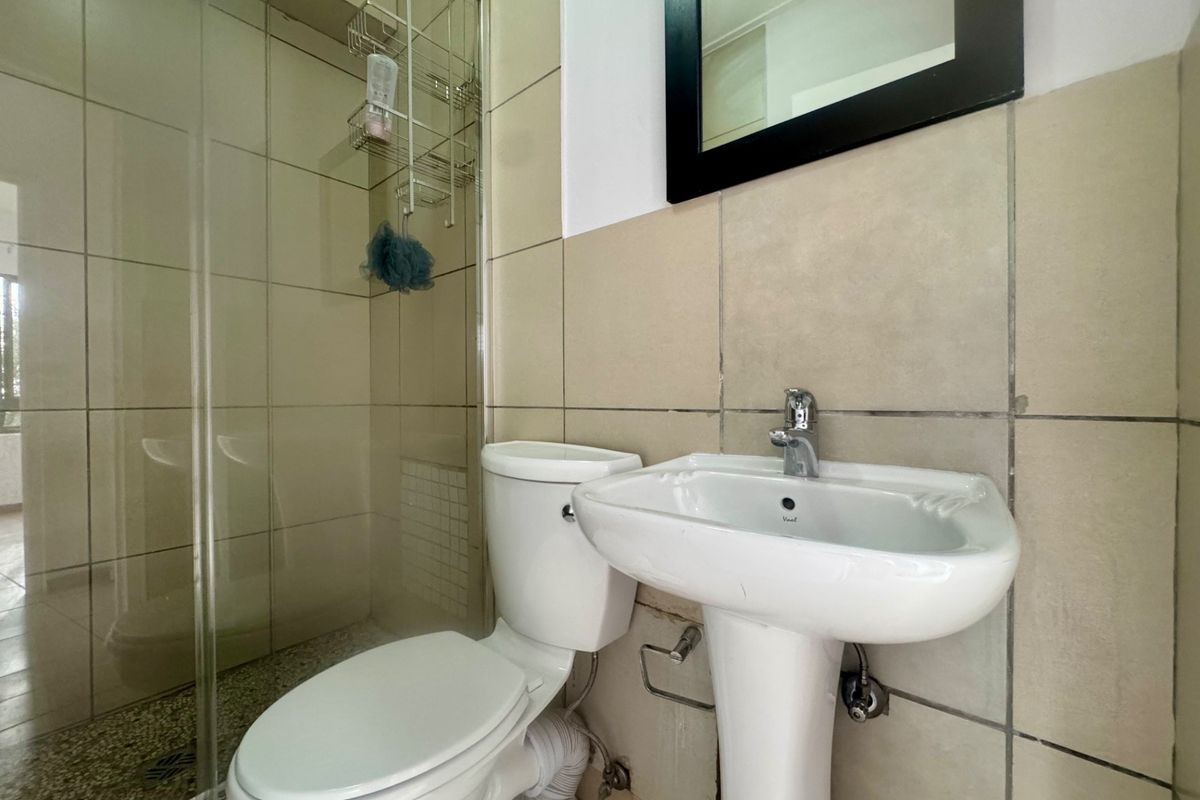 A functional bathroom featuring a pedestal washbasin, toilet, and a glass-enclosed shower with neutral ceramic wall tiling.