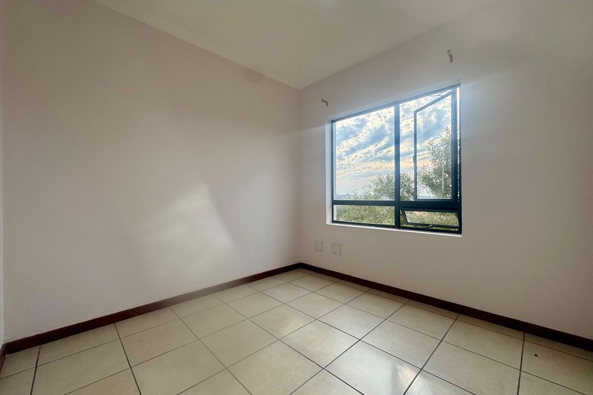 An empty bedroom featuring tiled flooring, neutral walls, and an aluminium window frame with natural light.