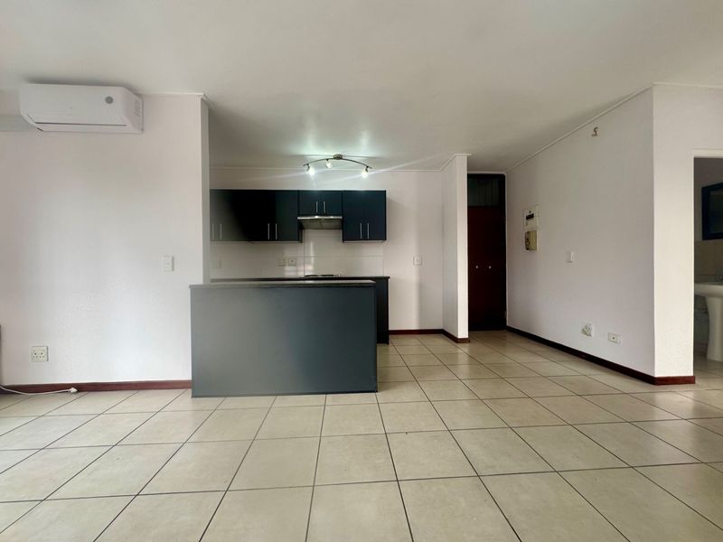 An open-plan living and kitchen area featuring dark cabinetry, a breakfast bar, tiled flooring, and a wall-mounted air conditioning unit.