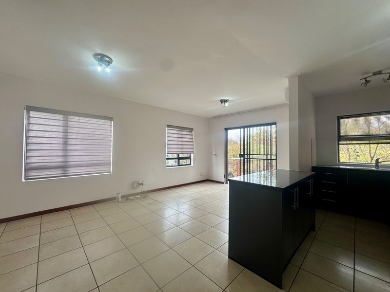 Spacious open-plan living area featuring tiled floors, a modern kitchen island, and direct access to a balcony through sliding glass doors.