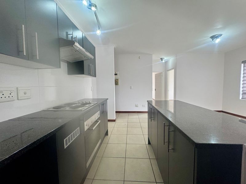 Modern kitchen featuring dark cabinetry, granite countertops, built-in oven, electric hob, and extractor fan, set against neutral tiled flooring.