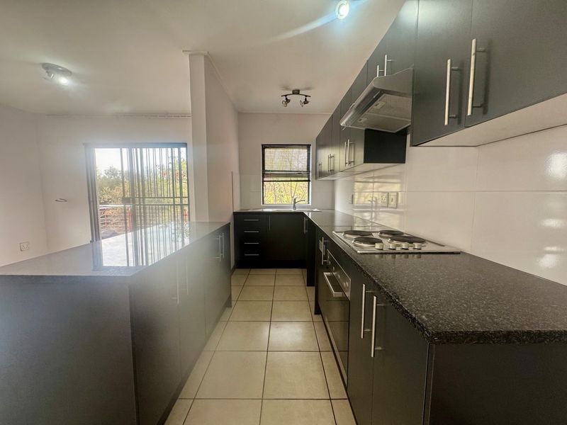 Modern kitchen featuring dark cabinetry, granite countertops, built-in electric hob, oven, and extractor fan, with tiled flooring and direct access to a balcony.