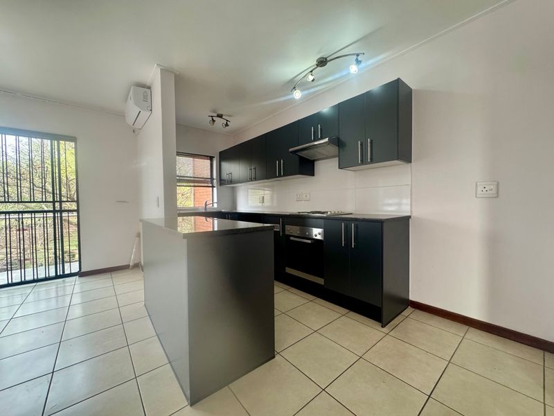Modern kitchen featuring dark cabinetry, granite countertops, built-in oven, hob, extractor fan, and tiled flooring, with an adjacent security gate leading to a balcony.