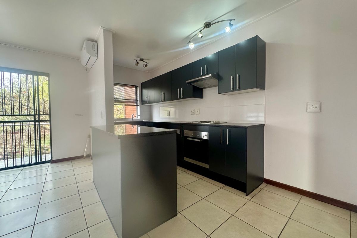 Modern kitchen featuring dark cabinetry, granite countertops, built-in oven, hob, extractor fan, and tiled flooring, with an adjacent security gate leading to a balcony.