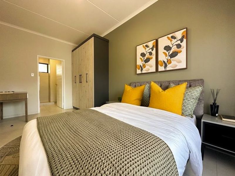 A well-maintained bedroom featuring a built-in wardrobe, neutral wall tones, and tiled flooring, with an adjoining doorway leading to an ensuite bathroom.