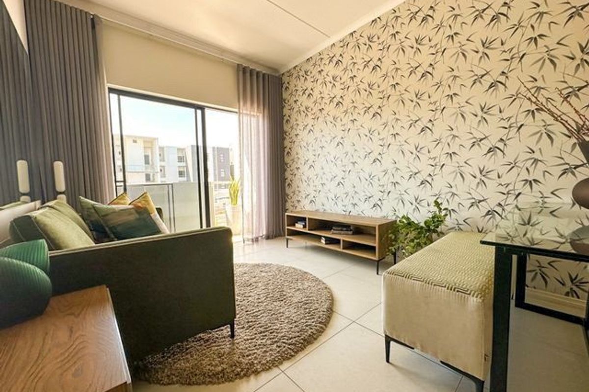 A bright living room featuring large sliding glass doors leading to a balcony, neutral tiled flooring, and a decorative feature wall.