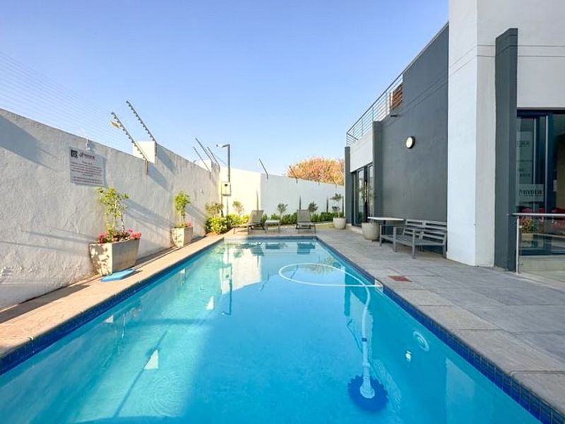 A well-maintained swimming pool area featuring paved decking, electric perimeter fencing, and direct access to the apartment via sliding glass doors.