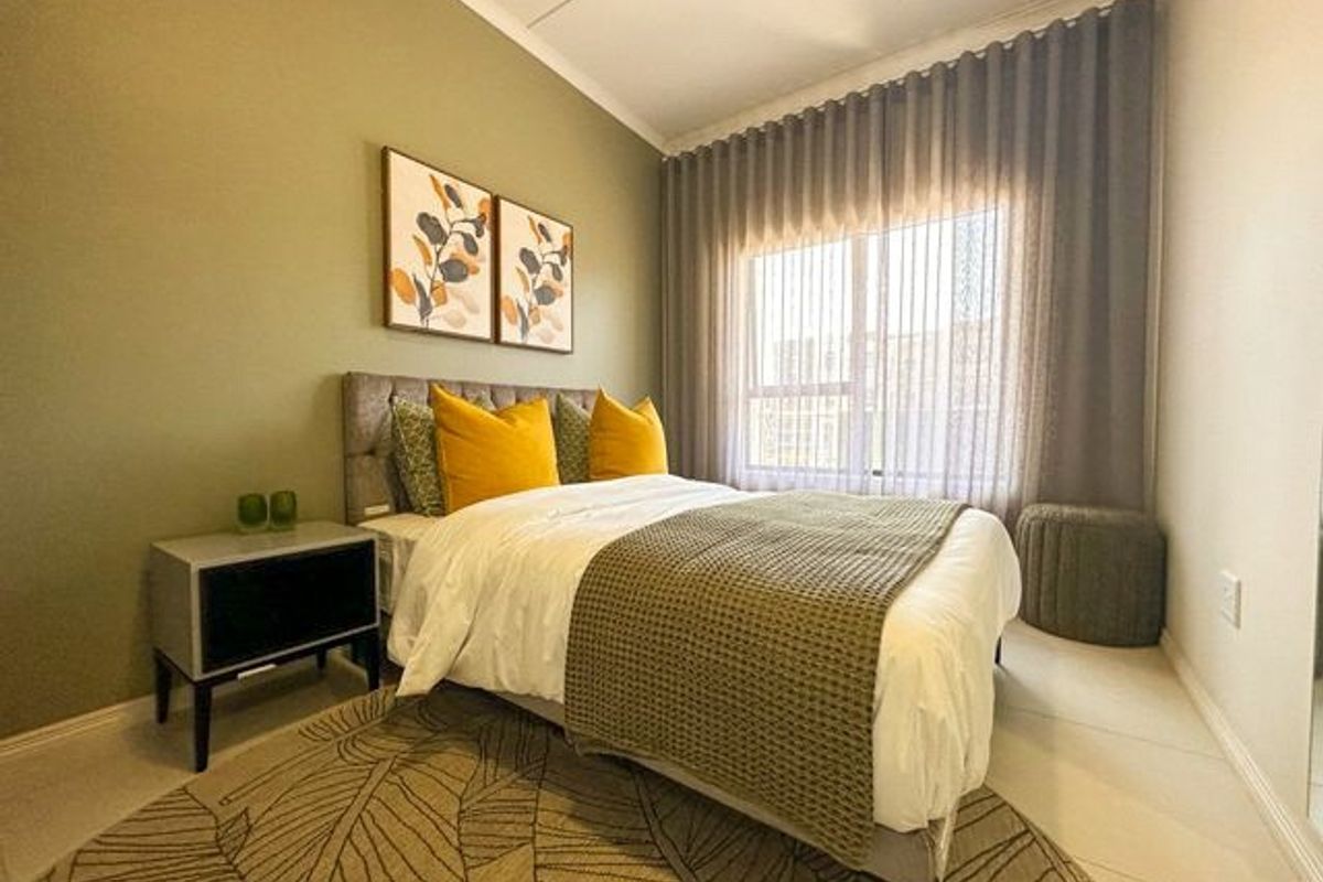 A well-maintained bedroom featuring neutral tiled flooring, soft green accent wall, and large window with floor-to-ceiling curtains providing natural light.