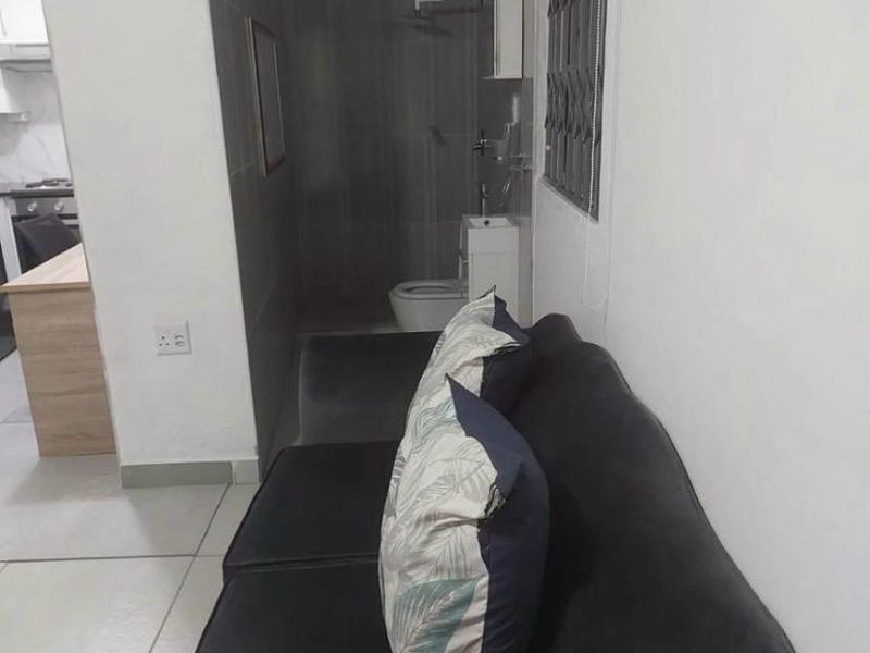 Open-plan living area featuring tiled floors, an integrated kitchen, and an adjacent bathroom with a shower, toilet, and basin.