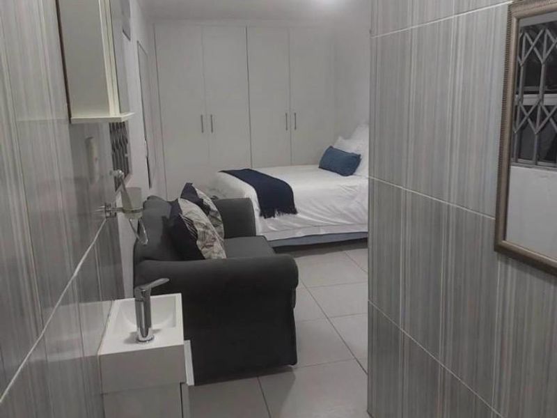 A bedroom featuring tiled flooring, built-in cupboards, and an integrated en-suite bathroom area with a wall-mounted basin and toilet.